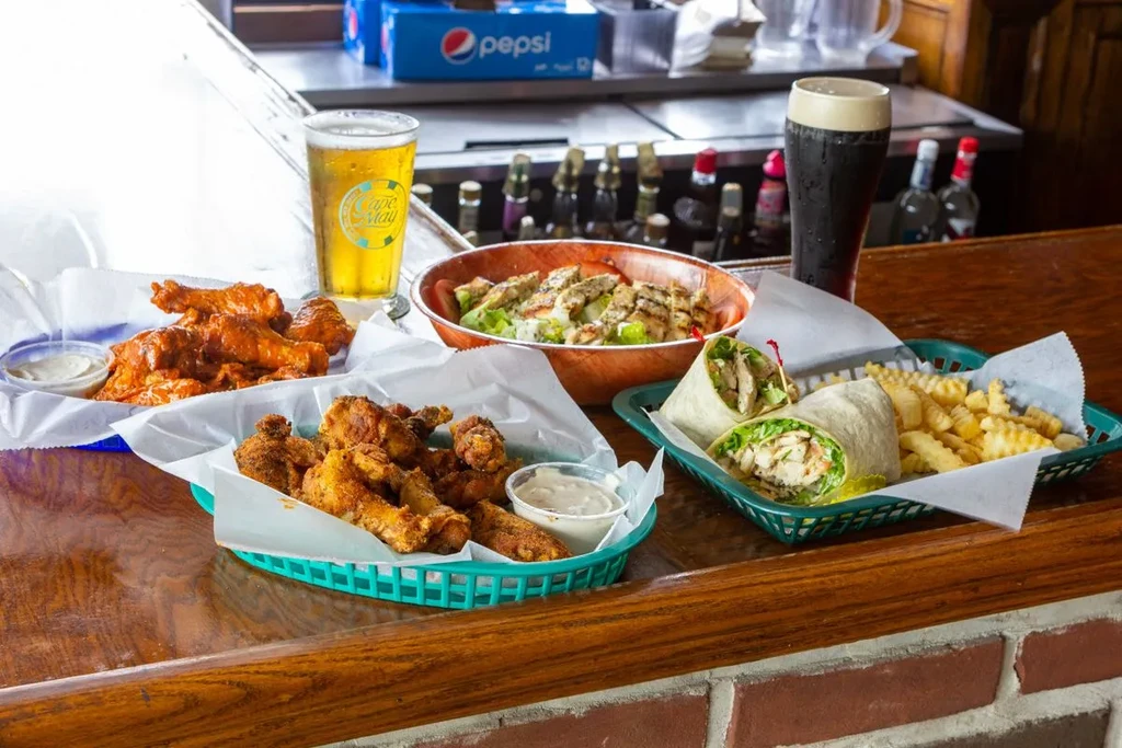 Wings, wrap, fries, salad, and beers arranged on a casual bar counter.