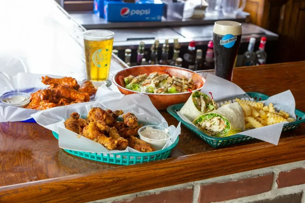 Chicken wings, wrap, salad, fries, and two beers on a wooden bar.