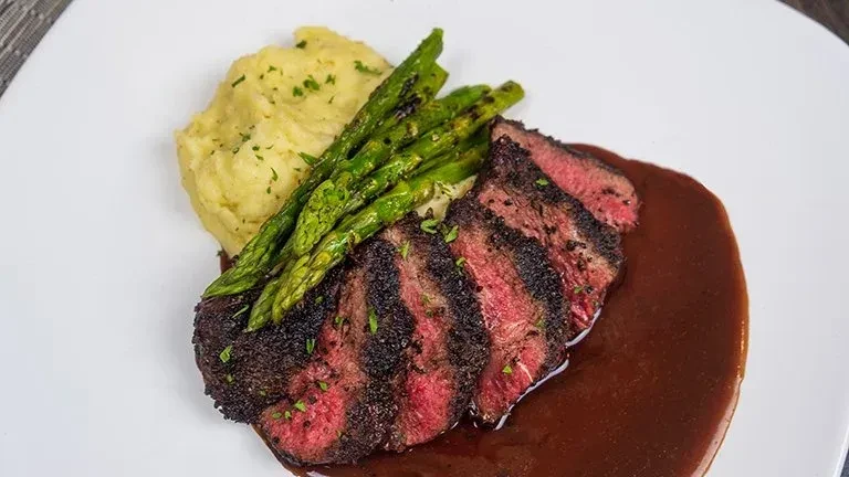 Medium-rare steak, mashed potatoes, asparagus, and dark sauce.
