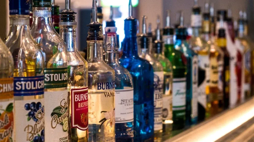 Numerous vodka and spirit bottles with spouts on a dimly lit bar.