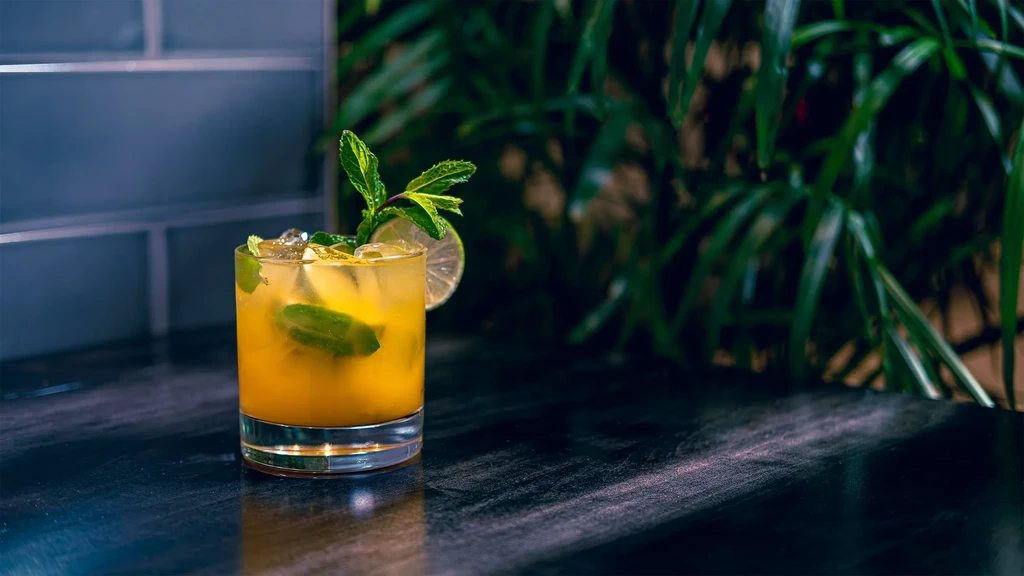Yellow-orange cocktail in a short glass with mint, lime, and ice.