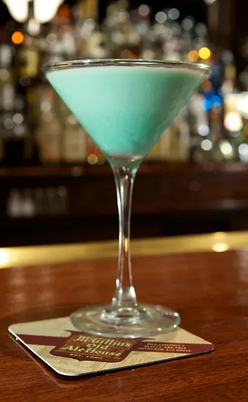 Martini glass with blue cocktail on bar, McGillin's Old Ale House coaster.