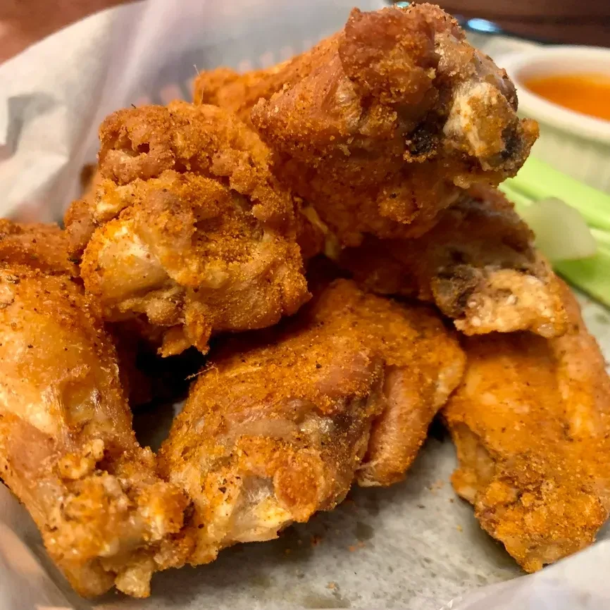 Seasoned fried chicken wings in a basket, dipping sauce, and celery.