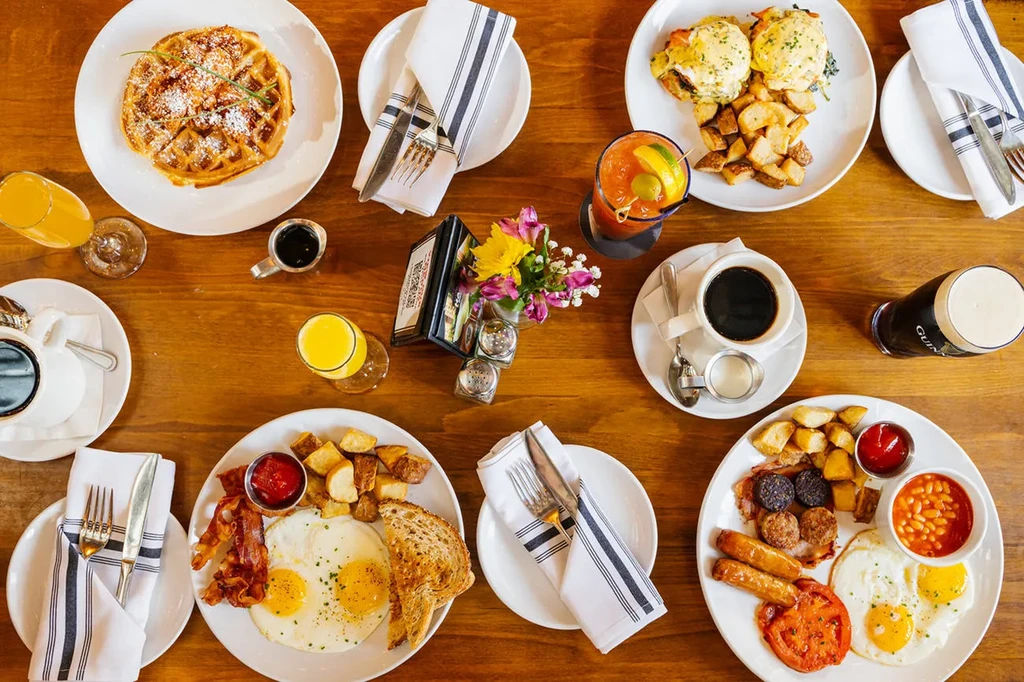 Overhead flat-lay of a wooden table with various breakfast and brunch dishes.