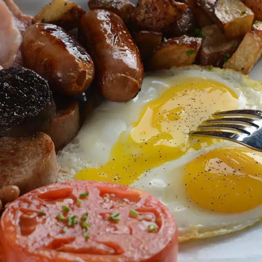 Full English breakfast with fried eggs, sausages, bacon, potatoes, and tomato.