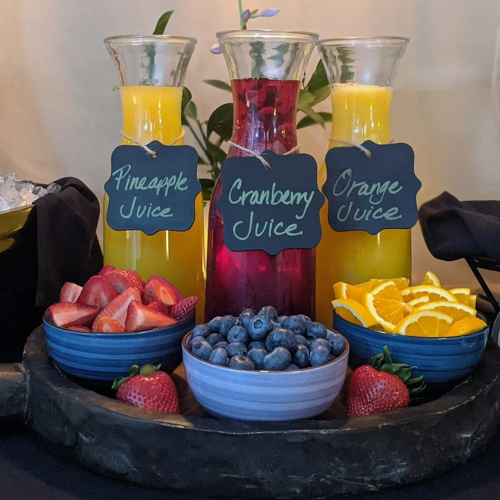 Carafes of colorful juices, bowls of fresh fruit on a wooden tray.