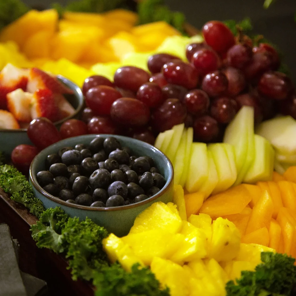 Fruit platter on dark board with grapes, blueberries, apples, and pineapple.