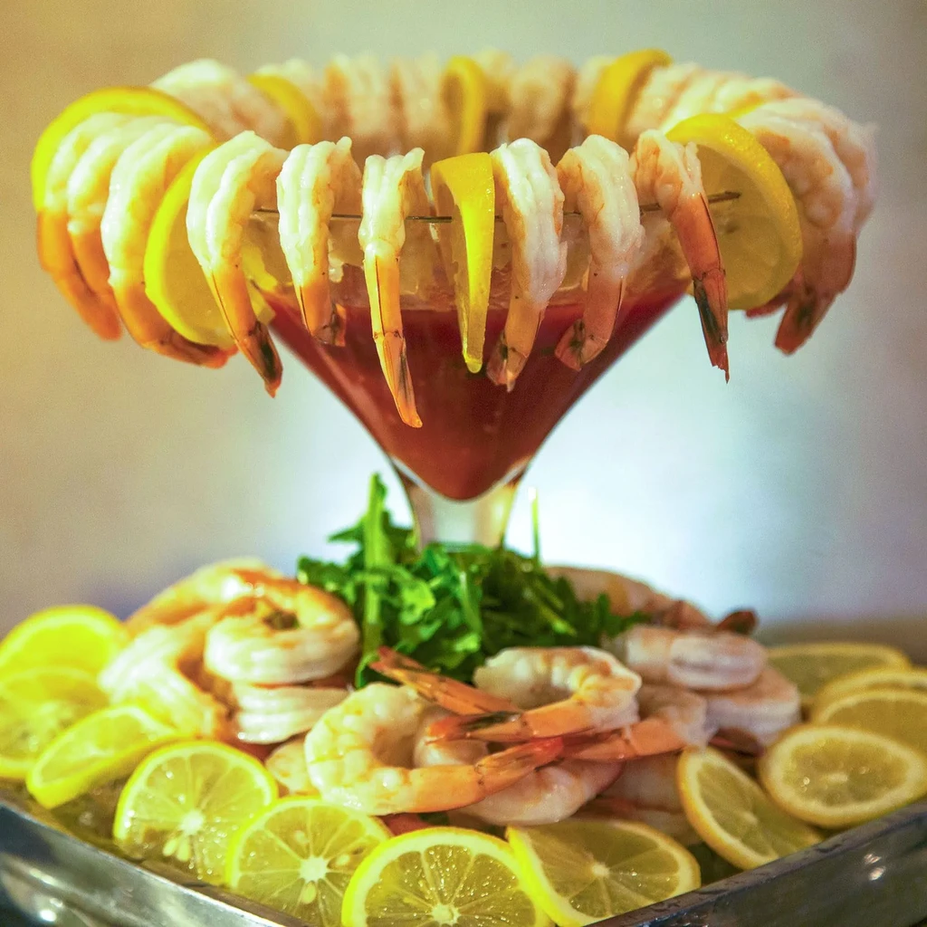 Shrimp cocktail with red sauce in martini glass, surrounded by lemons.