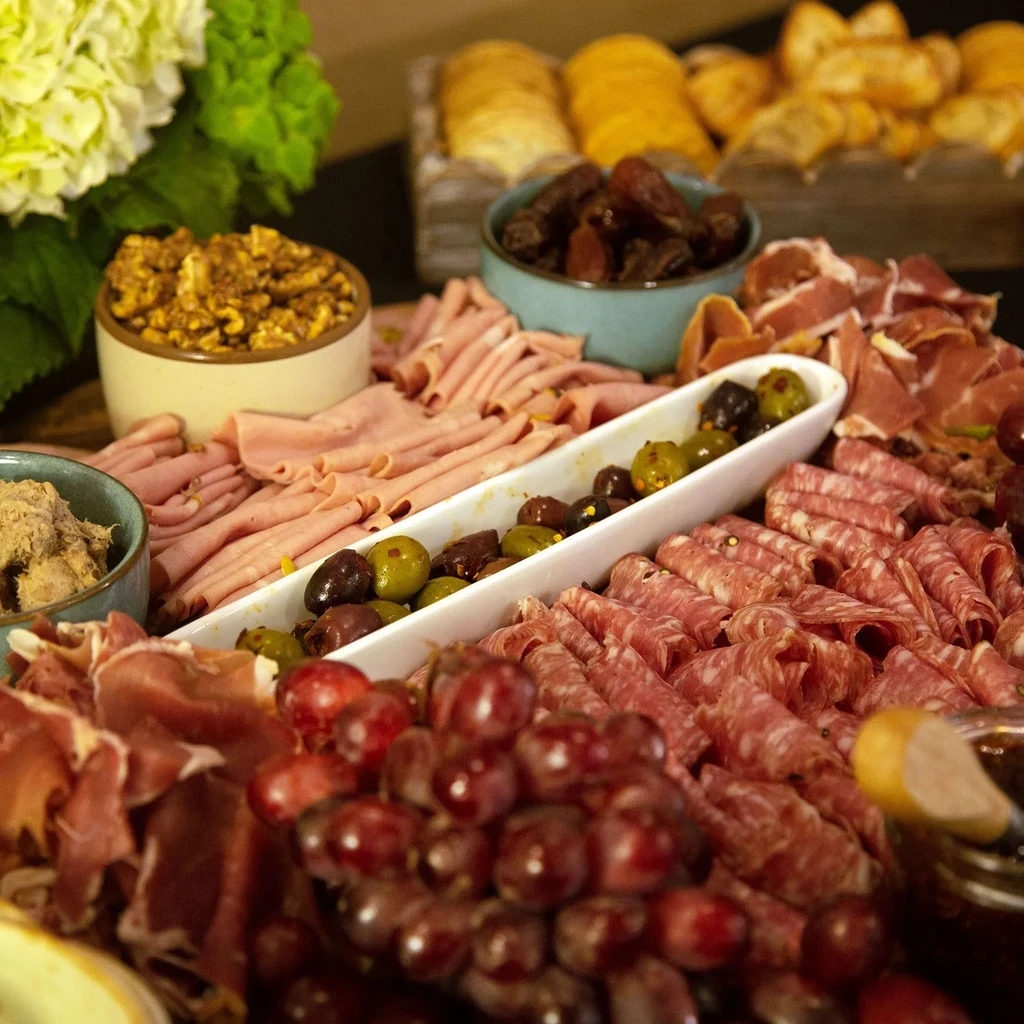 Abundant charcuterie board with sliced meats, olives, grapes, and various accompaniments.