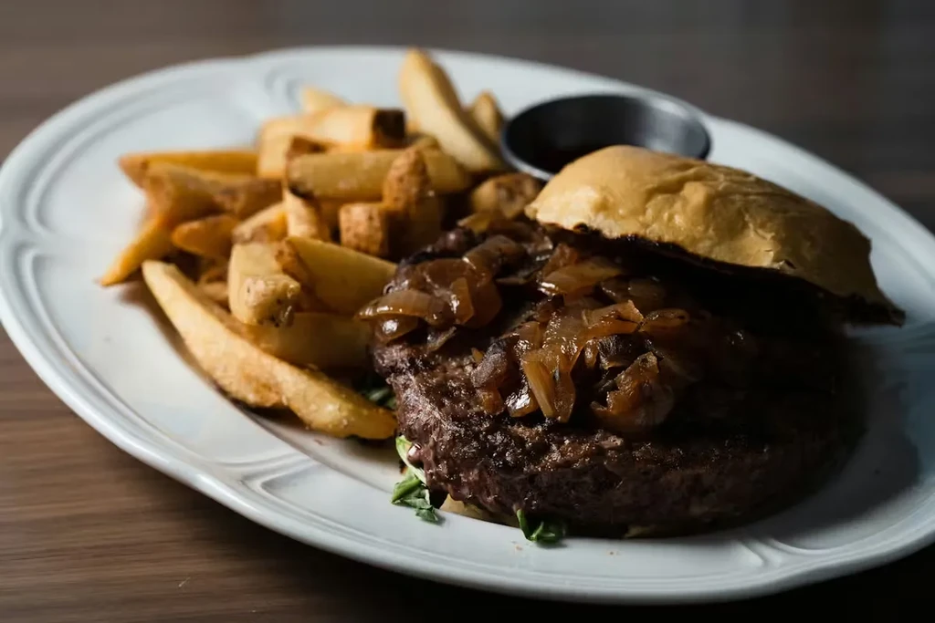 Gourmet hamburger with caramelized onions, fries, and dipping sauce.