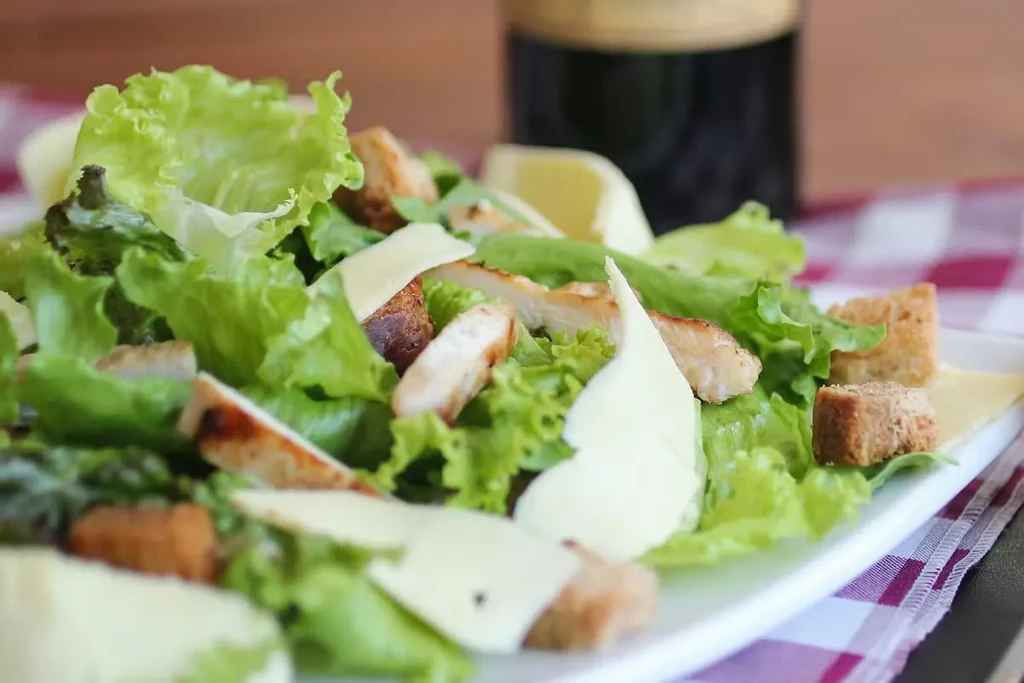 Close-up of Caesar salad with grilled chicken, croutons, Parmesan on white plate.