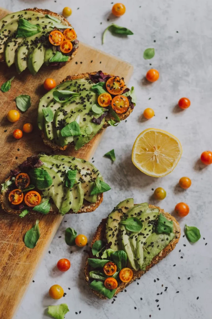 Four colorful avocado toasts with tomatoes, greens, and sesame seeds.