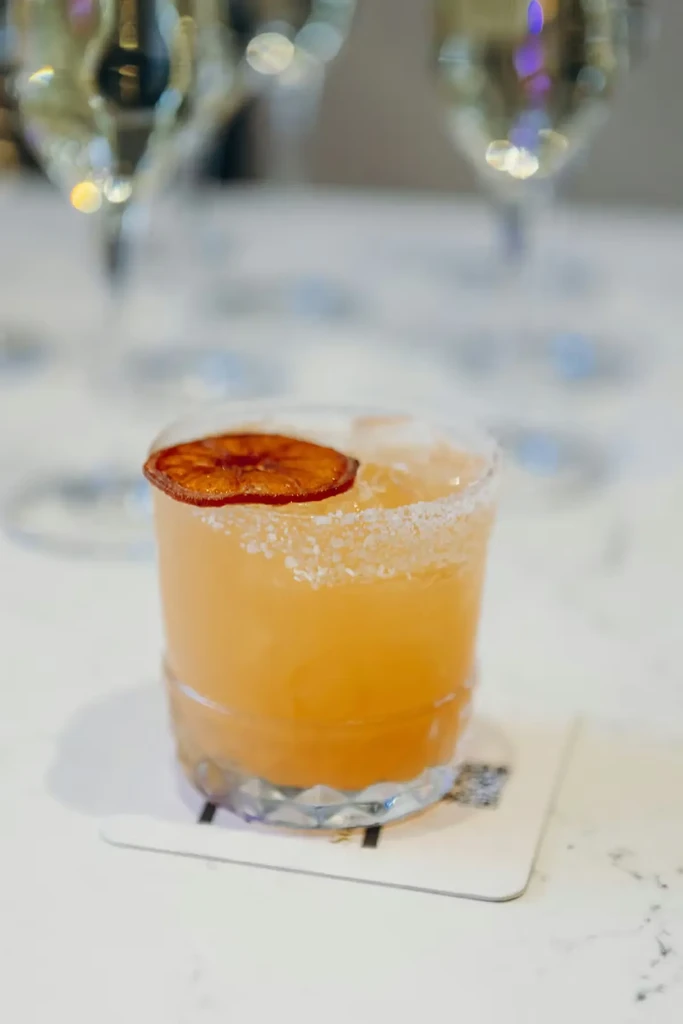 Frothy orange cocktail in faceted glass with salted rim and orange garnish.