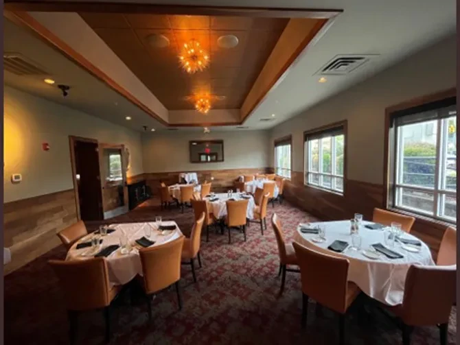 Empty upscale dining room with set tables and ornate starburst chandeliers.