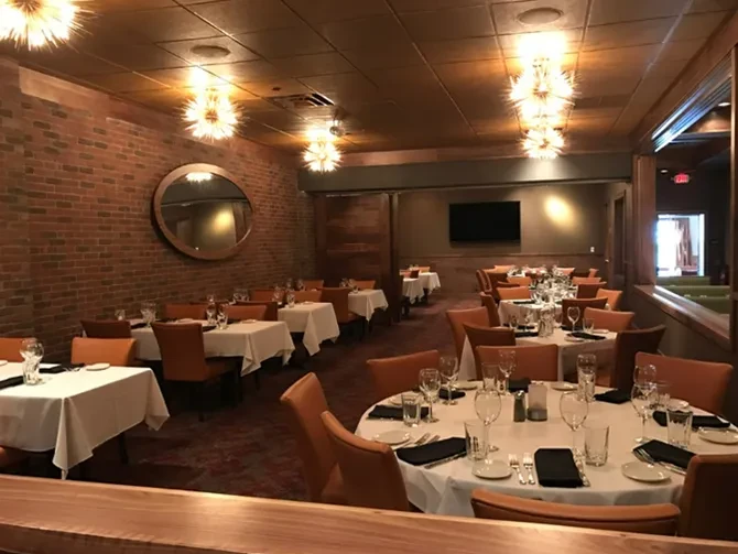 Restaurant dining area with set tables, spiky pendant lights, and brick wall.