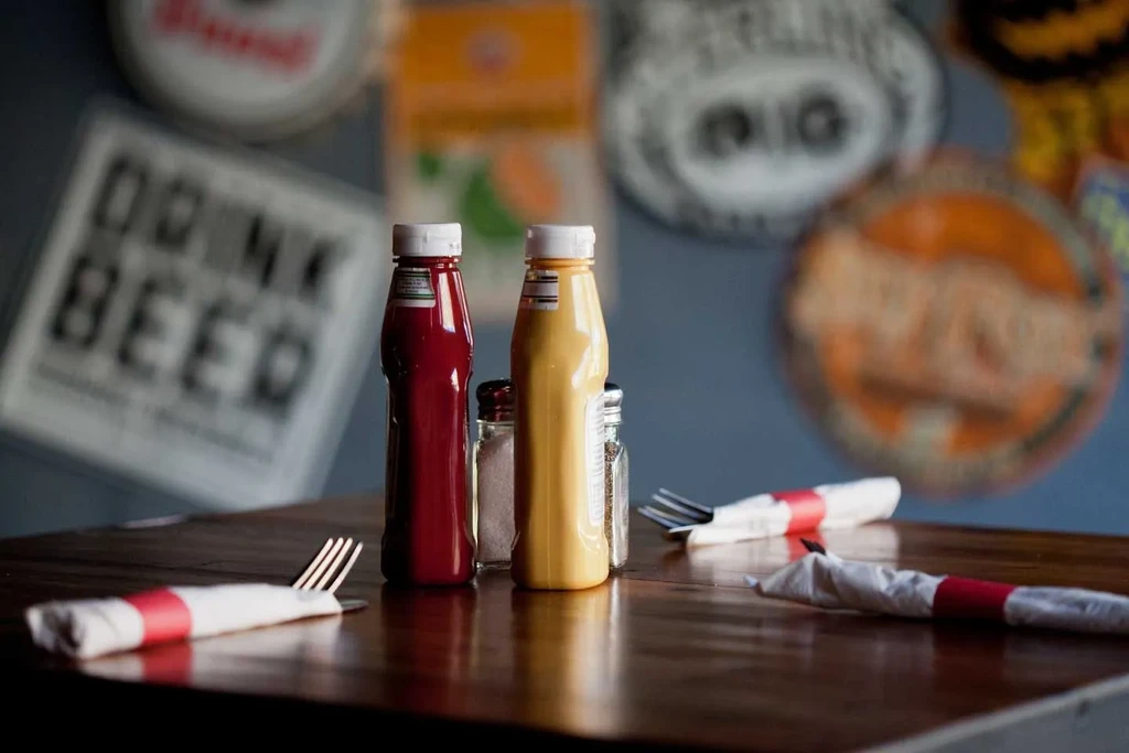 Ketchup, mustard, salt, pepper, cutlery on a wooden restaurant table.