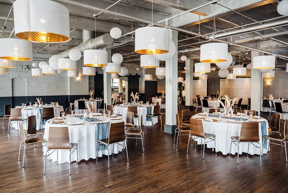 Modern elegant event space with set dining tables and industrial ceiling.