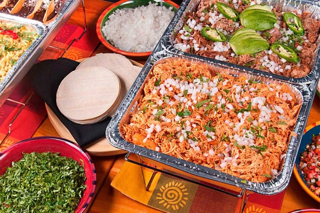 Mexican buffet with shredded meat, chicken, tortillas, and colorful garnishes.