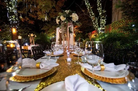 Outdoor dining tables with gold sequin runner, white flowers, and fairy lights.