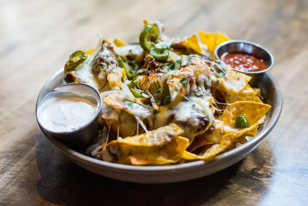 Cheesy nachos with chicken, jalapeños, and sides on a wooden table.