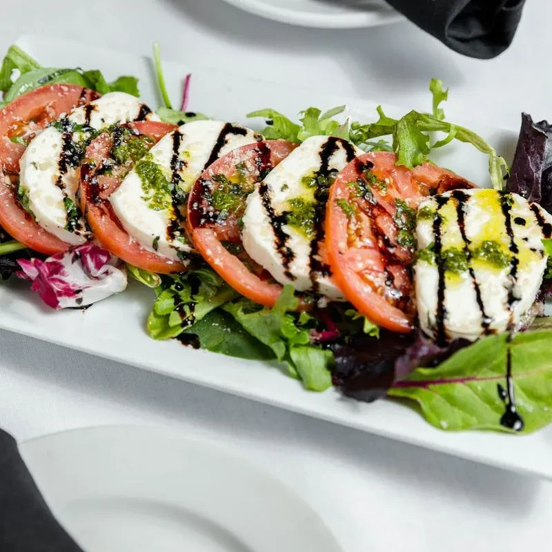 Caprese salad with alternating tomato, mozzarella, pesto, and balsamic glaze.
