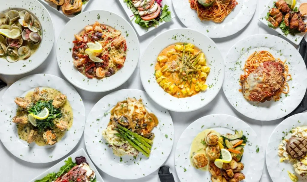 Overhead view of many vibrant Italian and Mediterranean dishes on white.