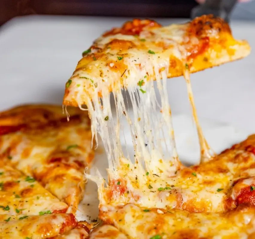Pizza slice lifted, showing long, melted mozzarella cheese and green herbs.