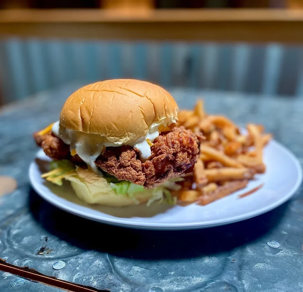 A crispy fried chicken sandwich with lettuce, creamy sauce, and french fries.