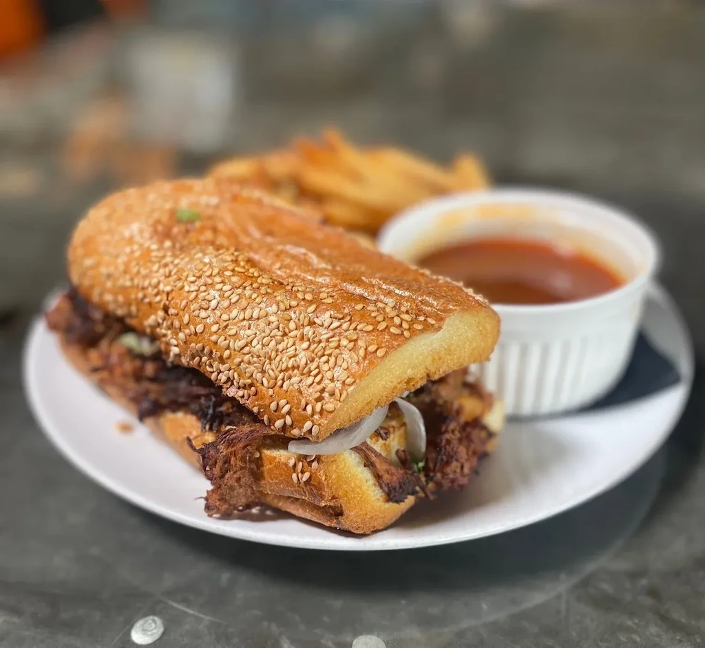 Sesame seed sub sandwich with shredded meat, fries, and sauce.