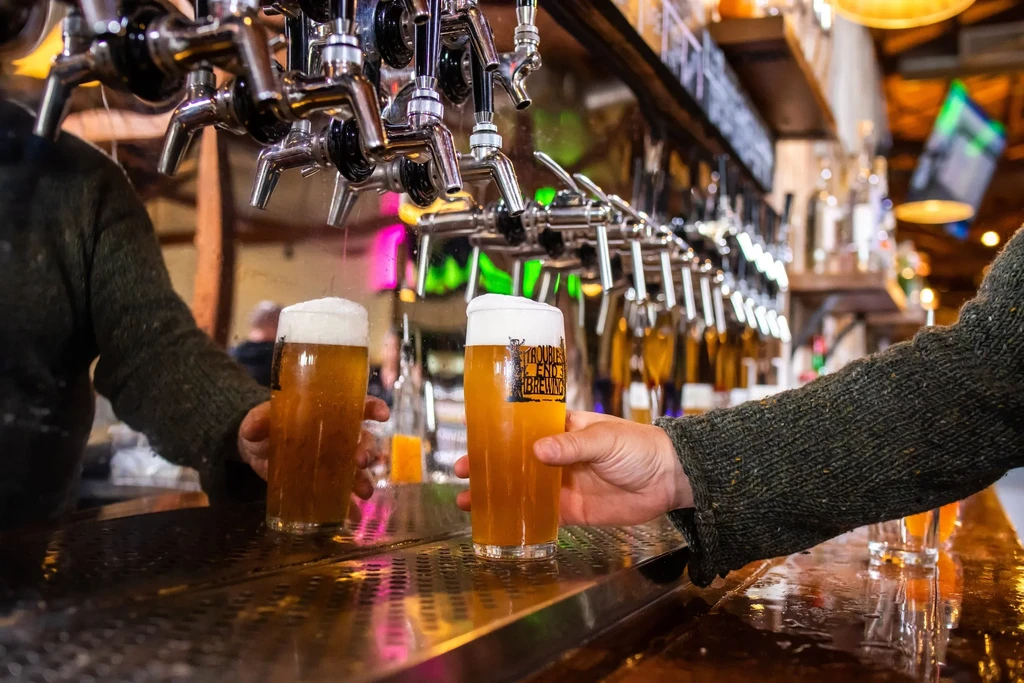 Two glasses of beer and many taps in a cozy bar.