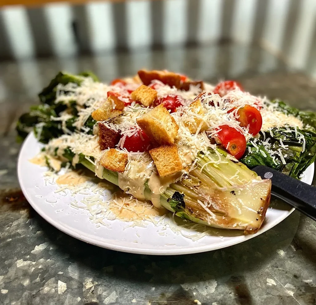 Halved grilled romaine lettuce with dressing, cheese, tomatoes, croutons.