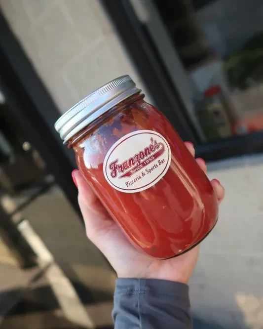 Hand holds Mason jar of Franzone's Pizzeria red sauce.
