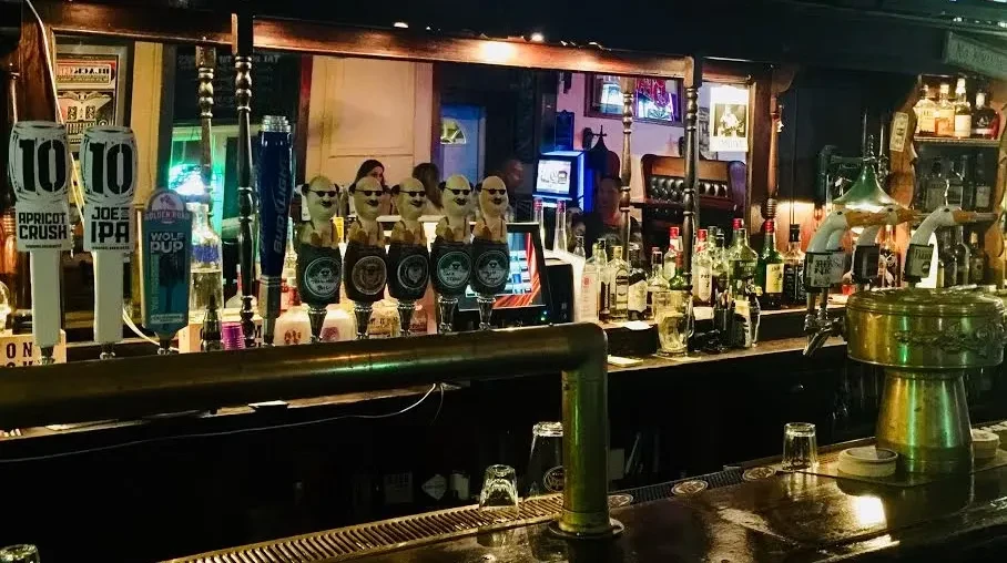 A dimly lit bar shows beer taps, liquor bottles, and a reflective counter.
