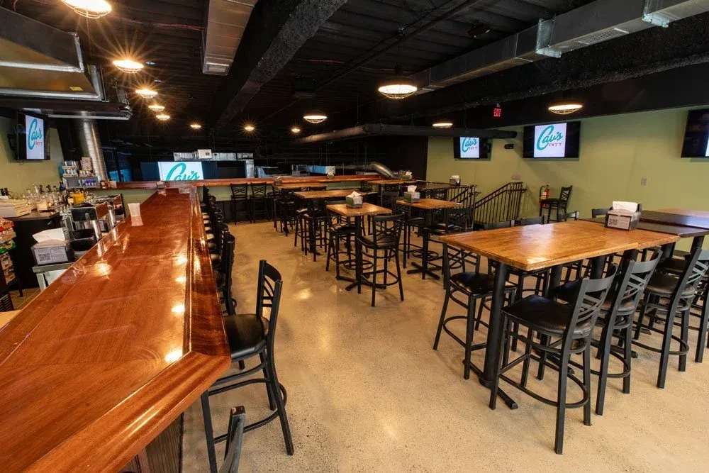 Empty modern bar with high-top tables, industrial lighting, and TVs.