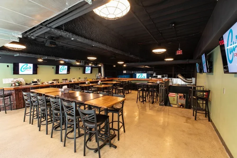 Empty modern restaurant interior with long bar, tables, and Cavi's TVs.