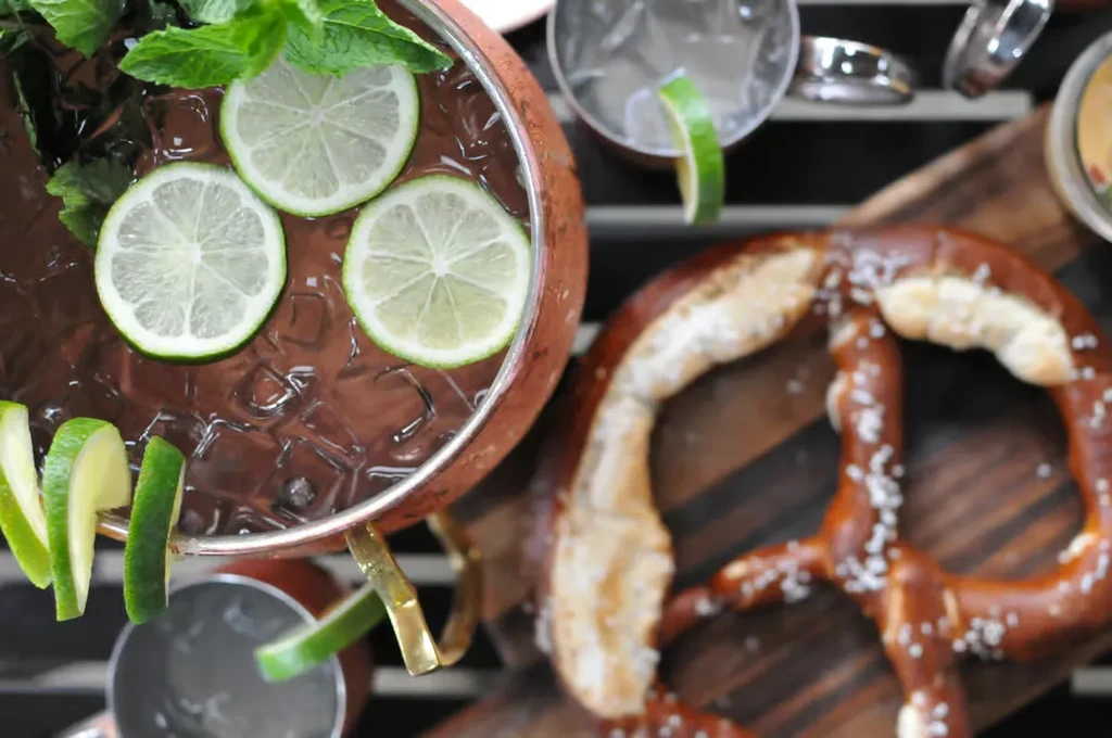 Copper Moscow Mule, lime, mint, and salted pretzel on wood.