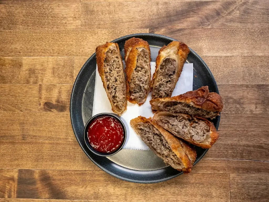 Golden-brown fried rolls with savory filling and red dipping sauce.