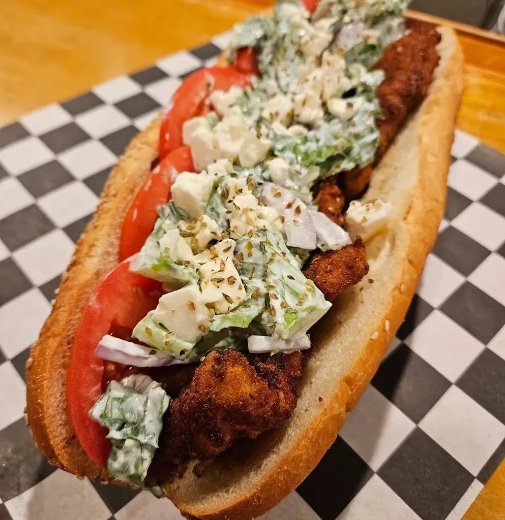 Close-up of a generously filled fried chicken sub with vegetables and cheese.