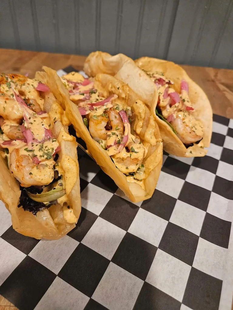 Three crispy shrimp tacos with pickled onions, creamy sauce, and herbs.