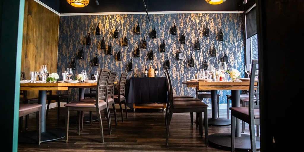 Restaurant dining room with mottled blue-gold wall, lanterns, and set tables.