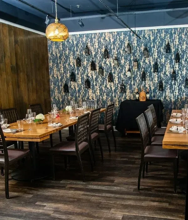 Empty restaurant dining area with patterned walls, wooden tables, and hanging lanterns.