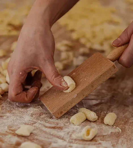 Close-up of hands shaping ridged pasta on a wooden gnocchi board.