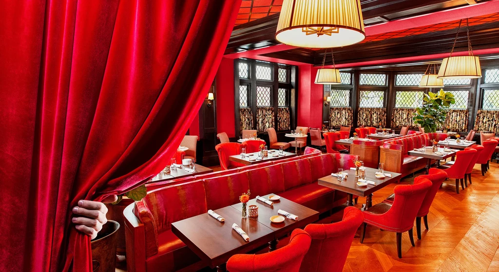 Warmly lit, red velvet restaurant with dark wood details, hand opens curtain.