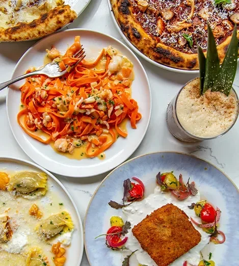 Overhead: restaurant table with pizzas, pasta, crispy item, and cocktail.