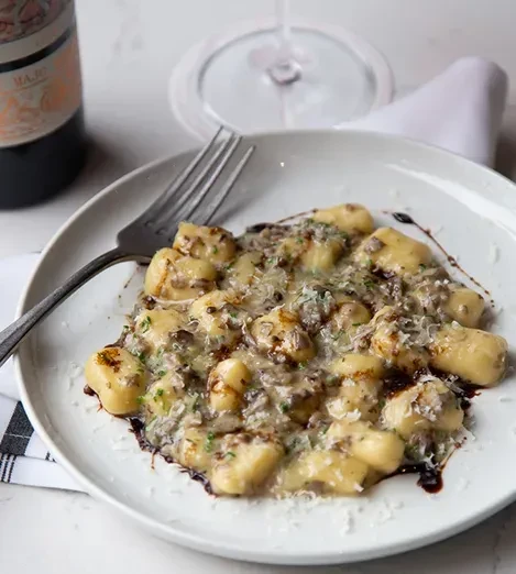 Gnocchi with creamy sauce, meat/mushrooms, cheese, herbs, in a dining setting.