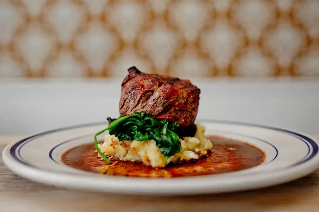 Seared steak with mashed potatoes, green vegetables, and sauce on a plate.