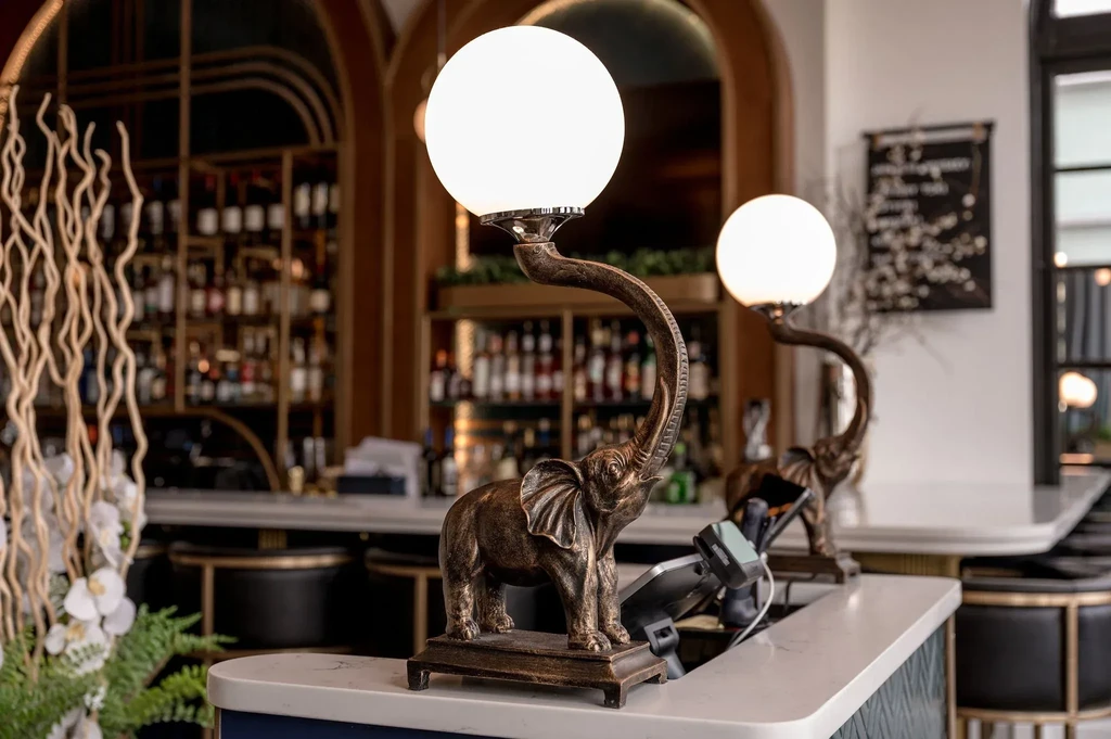 Ornate bronze elephant lamps on marble bar counter, stocked bar background.