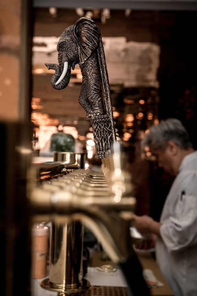 Ornate bronze elephant tap handle at a dimly lit bar.