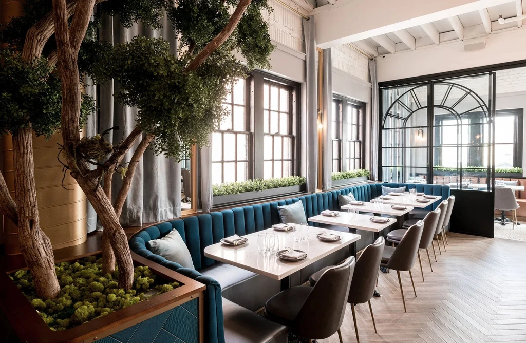 Bright, empty modern restaurant with teal banquette and artificial trees.