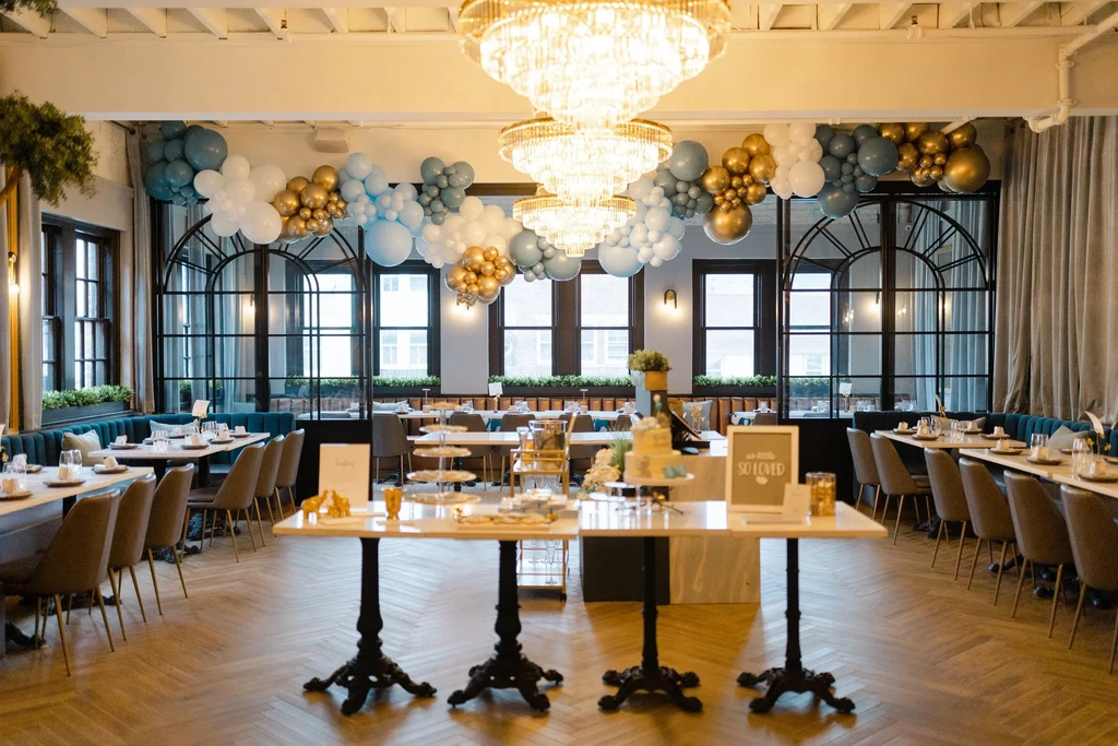 Celebratory event hall with chandeliers, balloon garlands, and dessert tables.